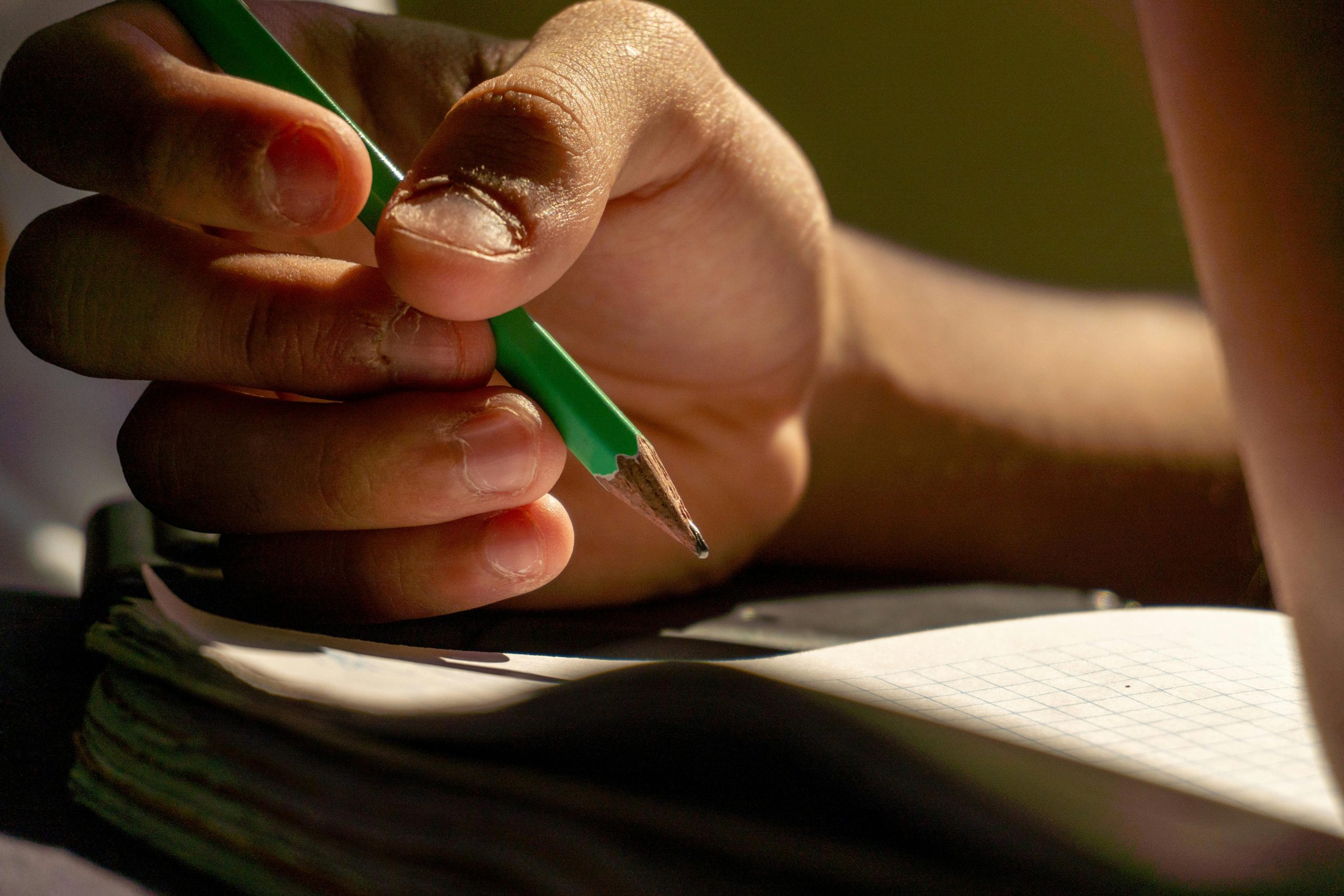 A person's hand holding a green pencil.